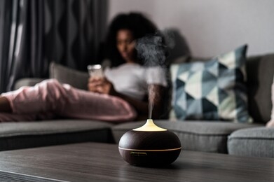 smart air humidifier emitting water vapor on table near sofa with black female at home
