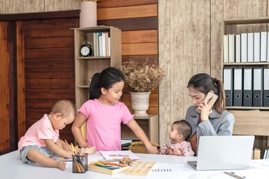 busy woman trying to work while babysitting three kids.  young asian mother on a call with three children playing around her . working women with multitasking.