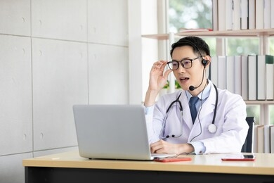 asian doctor talking with patient or co-worker through online video chat with computer in hospital