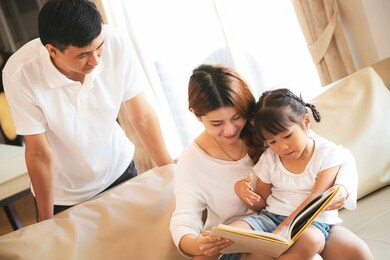 asian mother reading book to her daughter at home during home schooling 