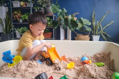 cute asian young boy playing with sand alone at home, kid playing with sand toys & toy construction machinery in urban home garden , montessori education, creative play for kids concept