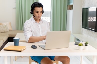 telework concept - asian man wear headset use laptop to join a video meeting at home freely