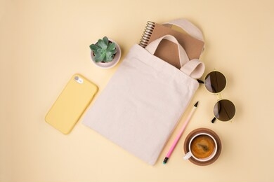 mockup design bag concept. top view of blank white tote bag canvas fabric with sunglasses and cup of coffee. cloth shopping sack mockup with copy space. yellow background.
