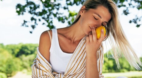 beautiful blonde young woman enjoying smells of lemon while resting in the park on sunlight. female on a picnic having a detox with citrus.