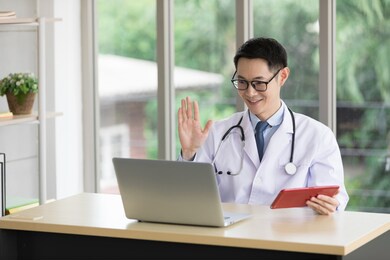 asian doctor say hello to patient or colleague with laptop computer having video conference at hospital
