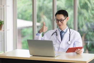 asian doctor talking with patient or colleague through online video chat with computer in hospital