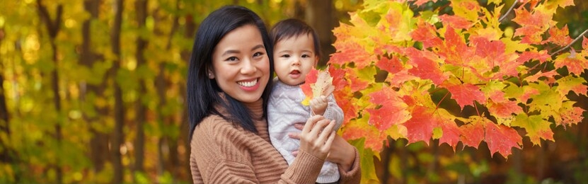 asian chinese mother with baby girl in autumn fall park. outdoor seasonal nature with yellow red leaves trees. halloween or thanksgiving autumnal holidays. web banner header.