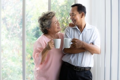happy senior couple looking into each other eyes smiling while enjoy drinking their morning coffee at home.