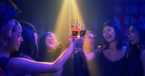 toasting glasses of wine in hands of asian woman and friends enjoy party in nightclub and toasting wine together to celebrate friendship with spotlight in dark background selective focused