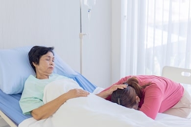 a sick mother in bed, asian woman rubbed her daughter's head asleep in the hospital bed