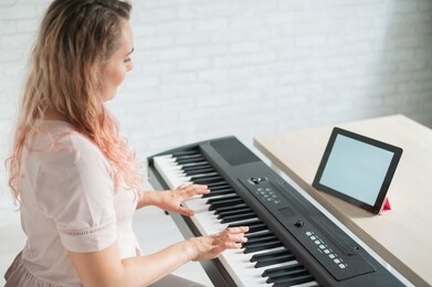 a woman watches video lessons on a digital tablet and plays on an electro synthesizer. the girl learns to play the piano remotely.