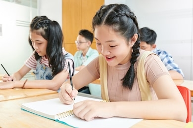 smiling asian school children writing in textbooks in class