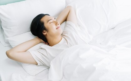 top view of young asian man smiling while sleeping in his bed and relaxing in the morning. rest relax good mood lifestyle concept.