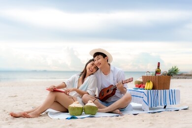 asian couple happy and enjoy the trip honeymoon of couple lover on the sea beach by playing ukulele and singing song music together. summer, holidays, vacation and happy people in thailand concept.