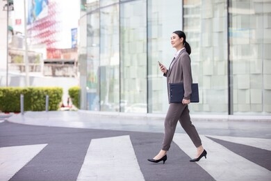 asian woman with smartphone standing against street blurred building background, fashion business photo of beautiful girl in casual suite with smart phone. 