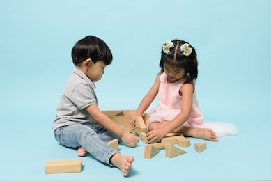 asian two people kids playing together to be enjoyable with wooden toys block on pastel blue background in studio. skill of children, childhood roles and birth order, child development concept.