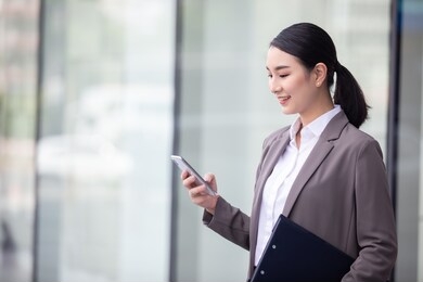 asian woman with smartphone standing against street blurred building background, fashion business photo of beautiful girl in casual suite with smart phone. 