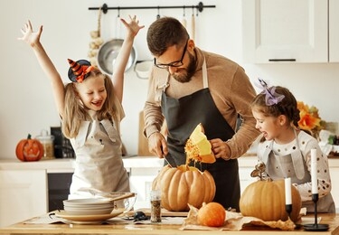 happy family   father  and children daughters prepare for halloween by carving pumpkins at home in the kitchen
