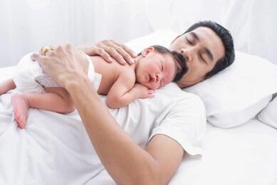 father with a baby at home sleeping. a portrait of a young asian father holding his adorable baby on white background.