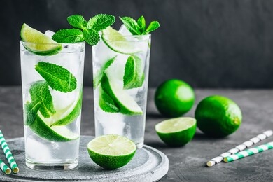 mojito cocktail with ice, fresh mint and lime in glass on dark stone background. refreshing ice cold summer drink.