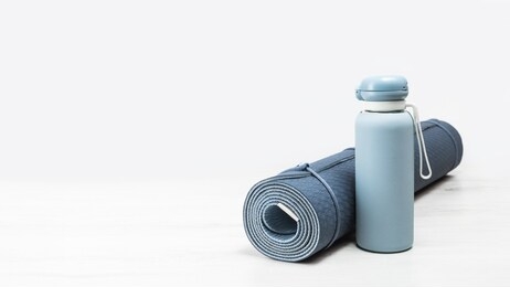 rolled blue yoga mat and blue water bottle on grey wooden surface. gender neutral fitness yoga and exercise concept with copy space. active lifestyle. workout at home or gym banner