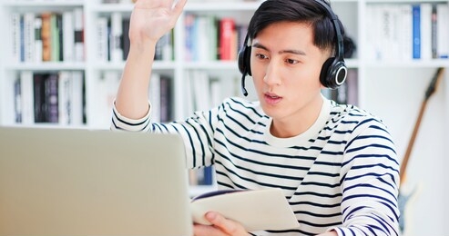 smart asian young male student use headset to study something at online courses and make discussion with laptop at home