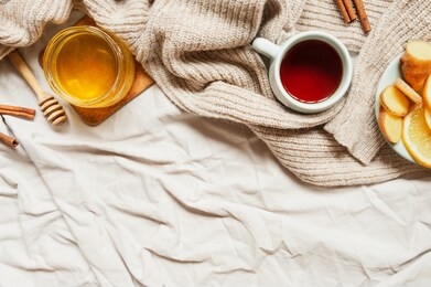 cozy autumn breakfast with tea, selective focus, honey, cinnamon sticks, lemon, ginger and a warm knitted sweater on a beige mint fabric