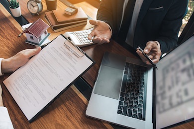 agents are using pens pointing to blueprint home design on laptop screen and being explained to customers at the office.