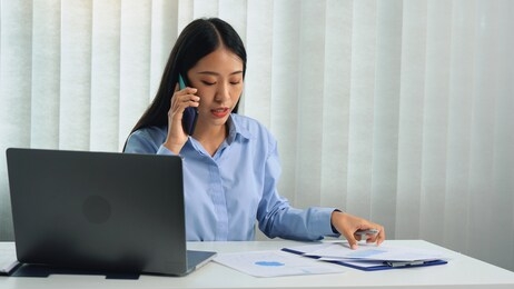 asian manager is on the phone with an employee and is furious at the office office's faulty paperwork.