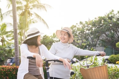happy senior asian woman cycling bicycle with daughter at park,health insurance and elder care concept