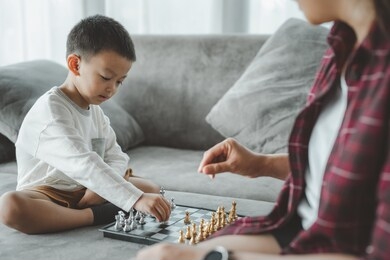 family hobbies. son playing chess with mother at home. little boy engaged in board game with his parent in room. asian people.