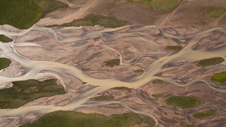 aerial top down glacial river texture structure milky river water and brown ground background with green grass icelandic moss covered islands, iceland