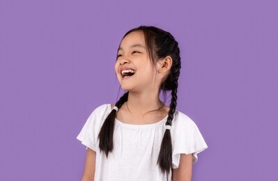 lol. joyful little asian girl laughing out loud posing over purple background. studio shot