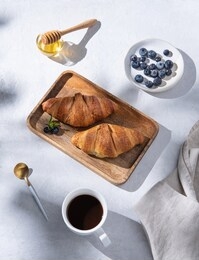 two  croissants on a cutting board  with cup of coffee, honey and  blueberries  on white table. top view