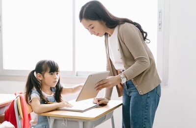 young asian female teacher helping schoolgirl with digital tablet in computer class. education, elementary school, learning and technology concept.