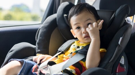 adorable asian kid boy (toddler age 1-year-old) protection sitting in the car seat with safety belt locked. family journey and baby careful concept. portrait closeup copy space, and blurry background.