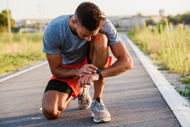 young handsome sporty jogger taking break from exercising outdoors looking on a smart fitness watch