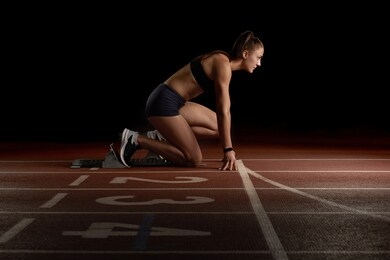 woman athlete sprinter preparing for start on the sport arena, black background