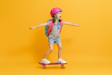 childhood and happy time! cute child with skateboard on color paper wall background. kid with backpack. girl ready to study.