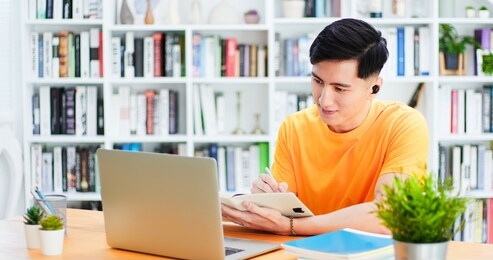 asian young male student use wireless earbuds to have online language courses by laptop at home   