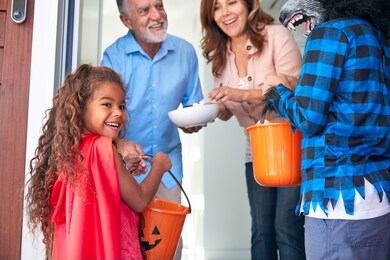 two children wearing fancy dress outside house collecting candy for trick or treat from grandparents