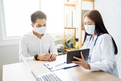 asian medical healthcare clinic doctor examining diagnosing male patient using tablet wearing surgical mask protection infection disease, working at home modern office technology computer laptop