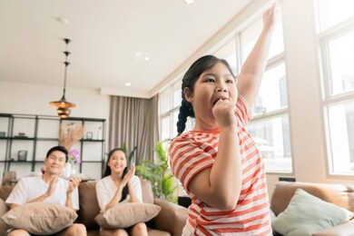 happiness pleasure asian lovely family enjoy watch and cheer up little daughter girl singing and dance practice in front of tv in living room 