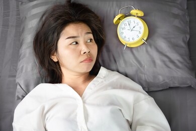 sleepless asian woman insomnia ,overthinking lying down in bed with alarm clock show the time late at night 
