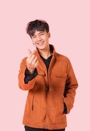 portrait of happy asian handsome young man in fashionable clothing and standing posing mini heart with smiling isolated on pink background.