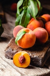 peaches with leaves on dark wooden board with peach in halves with peach seed stone. composition with ripe juicy peaches harvest for food. fresh organic fruit