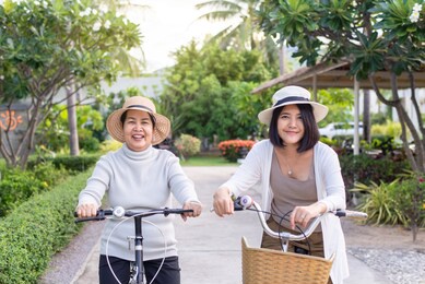 happy senior asian women cycling bicycle with daughter at public park,health insurance and elder care concept