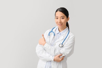 female asian doctor showing thumb-up on light background
