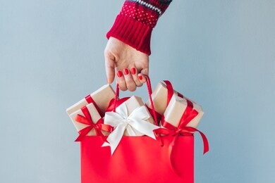 cropped image of female hand with red polished nails holding shopping bag full of christmas gift boxes. holiday sale concept. 