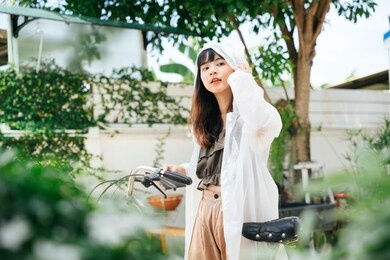 young asian woman wearing white raincoat walking at park with bicycle.